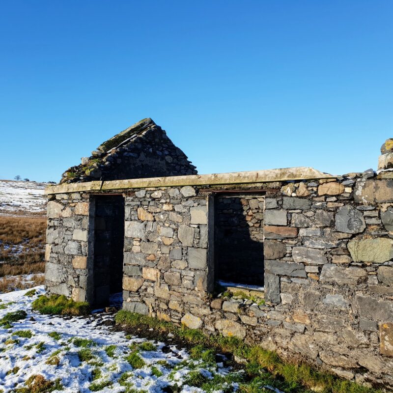A snowy ground. The old stone walls of an old building with no roof, a doorway with no door, and window with no glass.