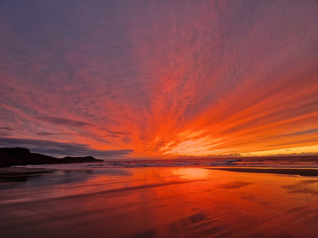 A sandy beach with the sunsetting over the sea.