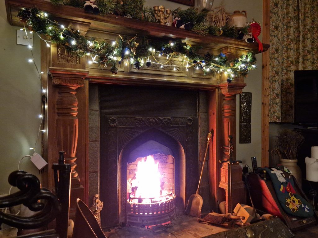 A roaring fire, with fairy lights and greenery around the fireplace