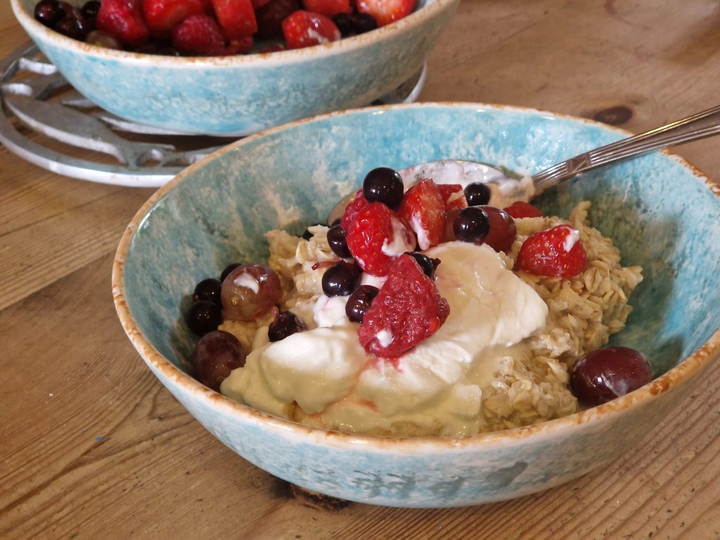 A bowl of porridge, fuit and yoghurt on a wooden table