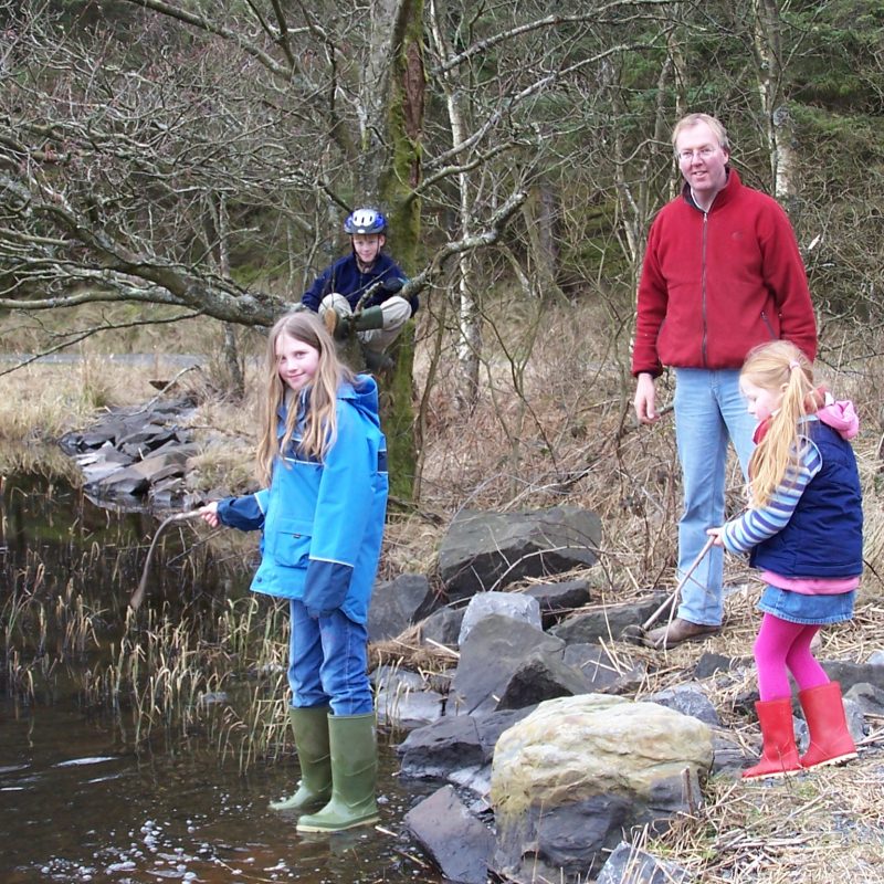 Man and children beside a loch in the woods