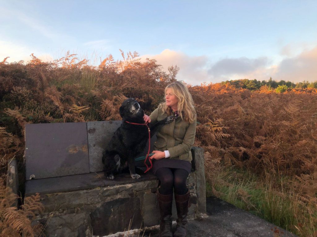 Woman on a slate bench with a dog sitting on the bench beside her.