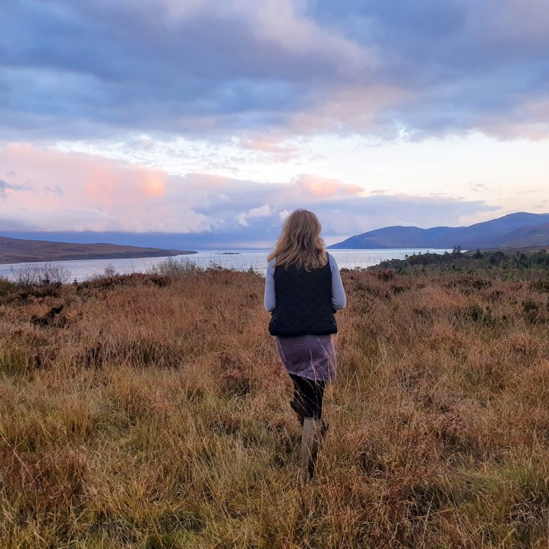 The back of a girl, stood on the hillside, looking out to sea