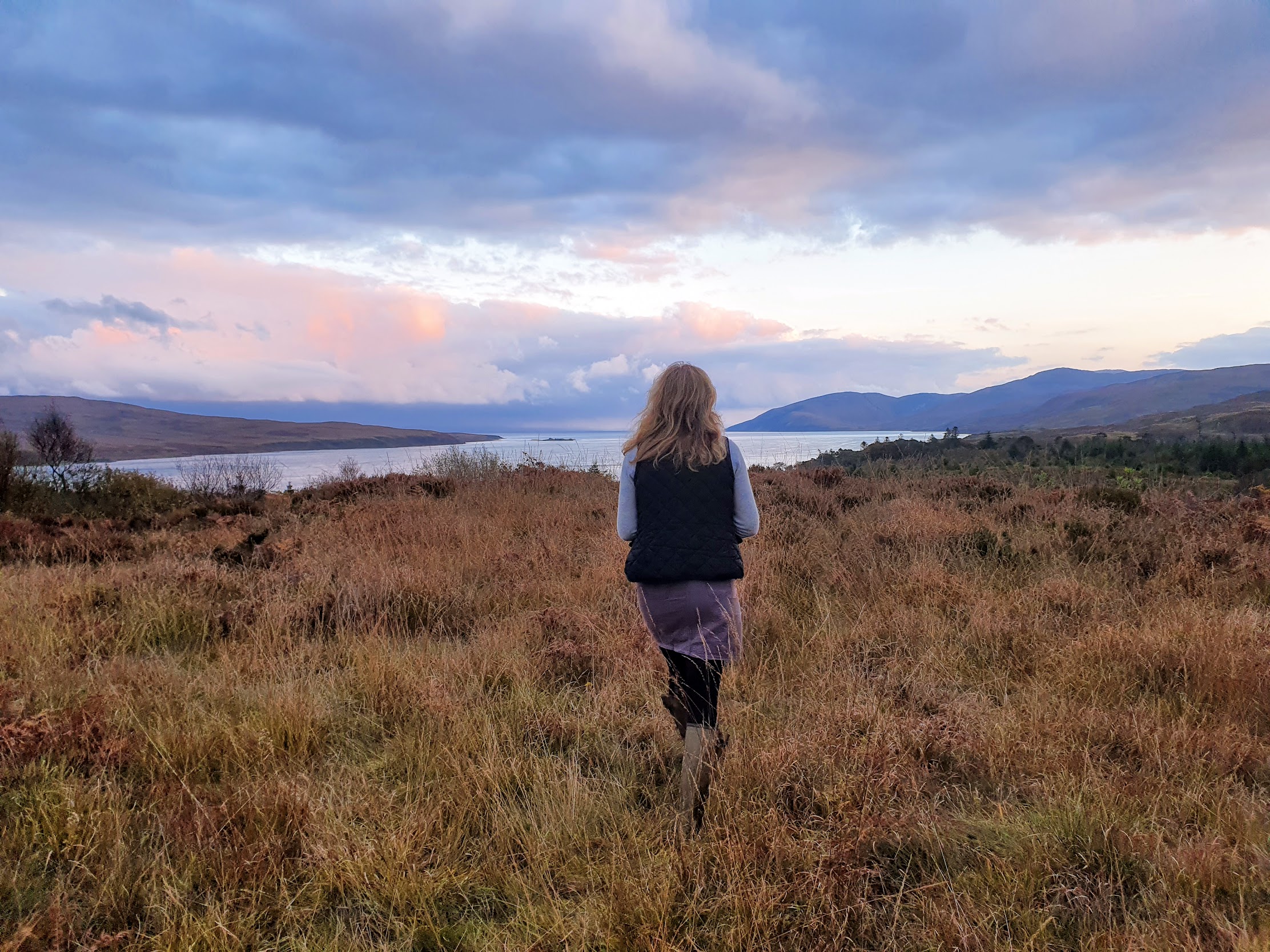 The back of a girl, stood on the hillside, looking out to sea