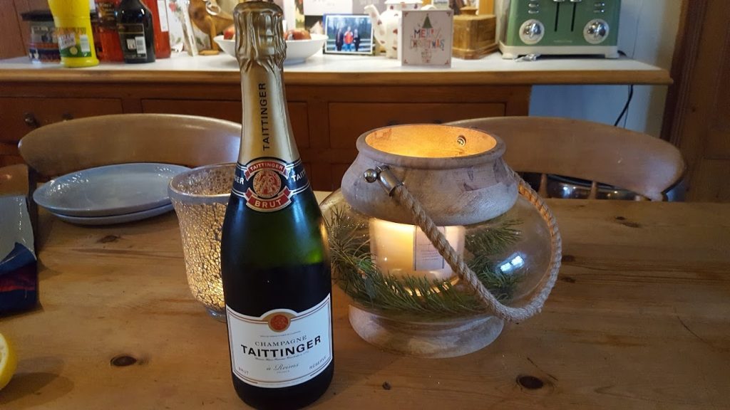 A bottle of champagne on a table ebside a candle
