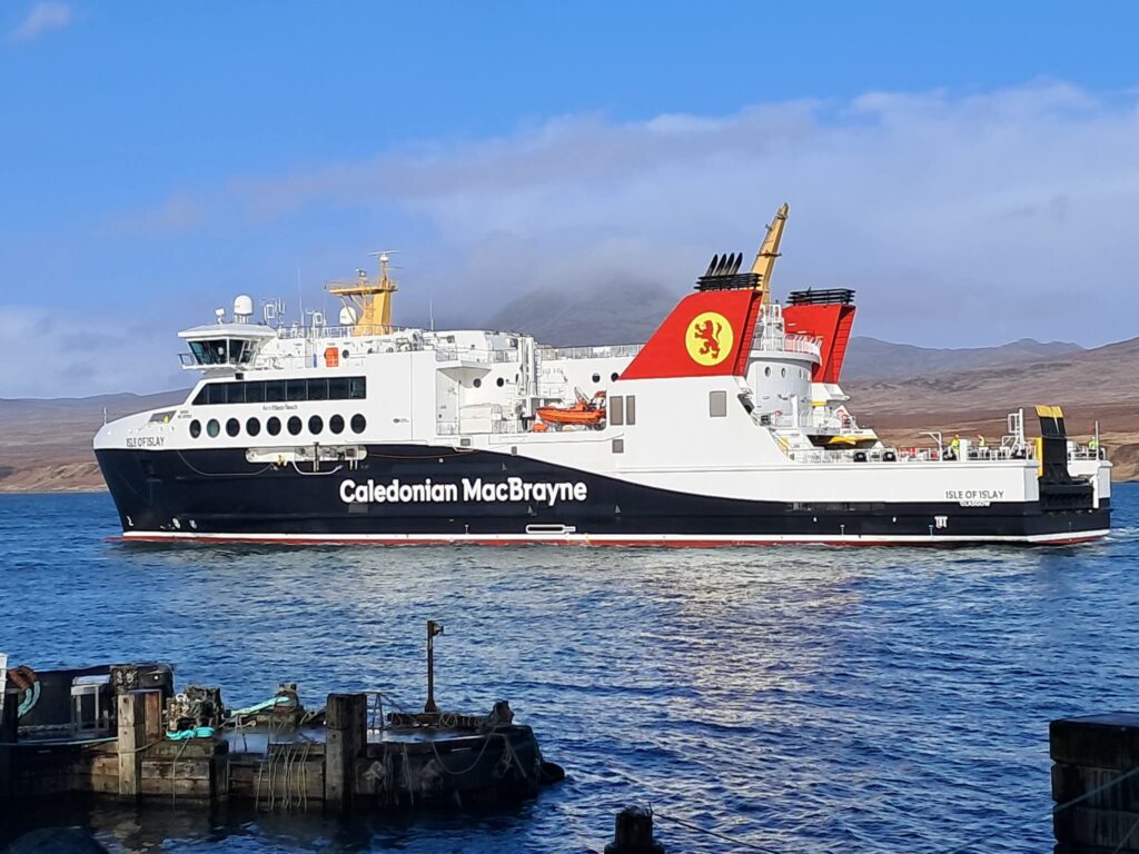 A large ferry boat on the sea with hills in the background and a jetty in the foreground
